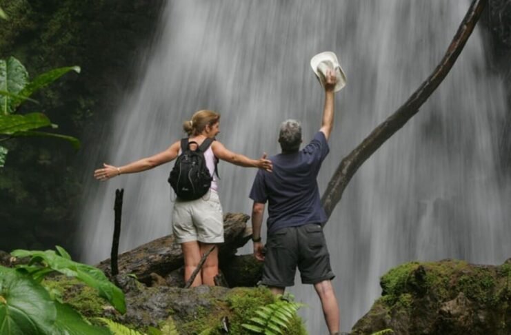 This image depicts a confident woman hiking through a verdant rainforest toward a cascading waterfall, embodying the essence of sustainable travel. She carries a lightweight backpack filled with eco-friendly gear, dressed in ethical activewear, surrounded by pristine natural scenery that highlights biodiversity conservation. The scene captures the empowerment of solo exploration in harmony with the environment, with soft sunlight filtering through the canopy to evoke tranquility and responsibility. Sustainable Travel Products Revolutionizing Women's Journeys